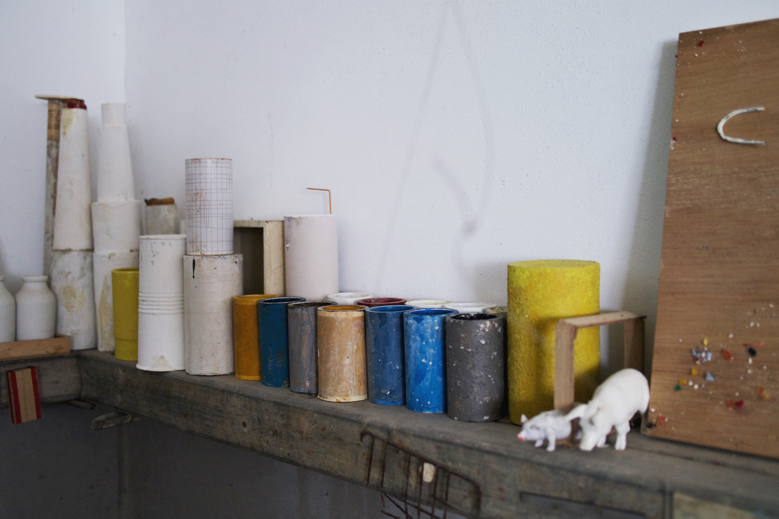 Recycled cylindrical forms in blue, gray and yellow lined on a shelf with white four legged animals blurred in foreground