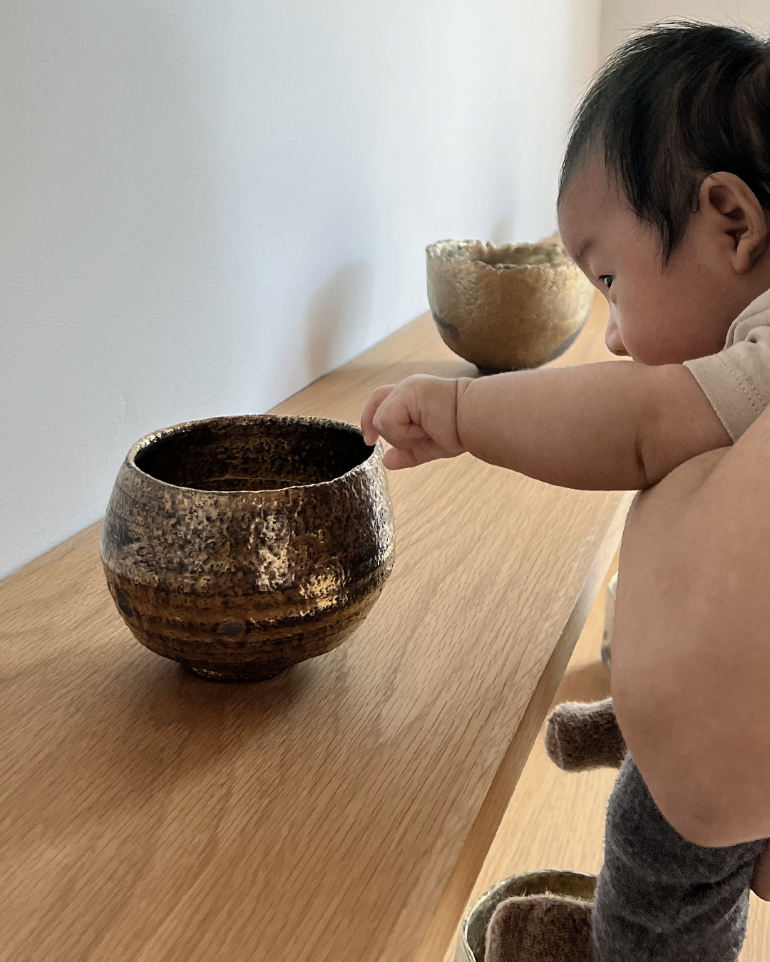 Gold chawan on display on wood shelf and baby touching it with one hand