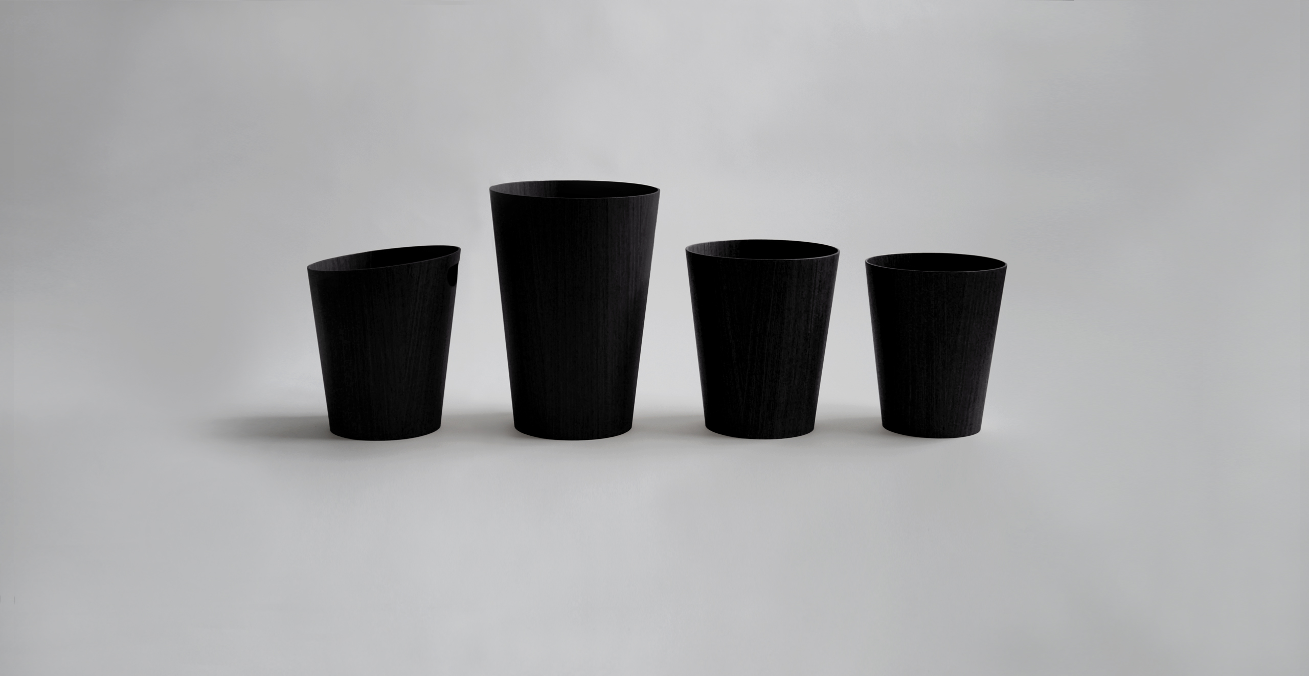 Four Saito Black Ash Wood waste baskets in a row in different styles against a light gray back drop
