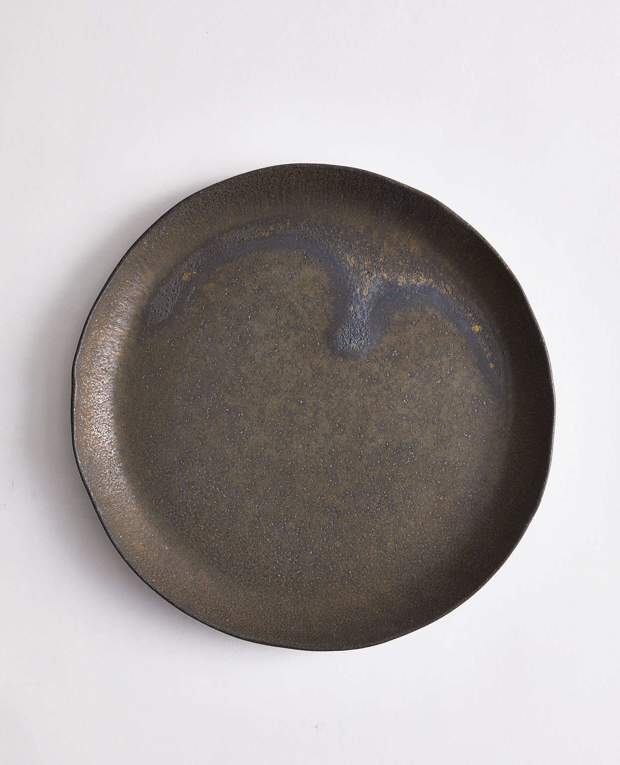 Black plate, with hints of bronze, blue, and brown due to the finish, by Keisuke Iwata on a gray background