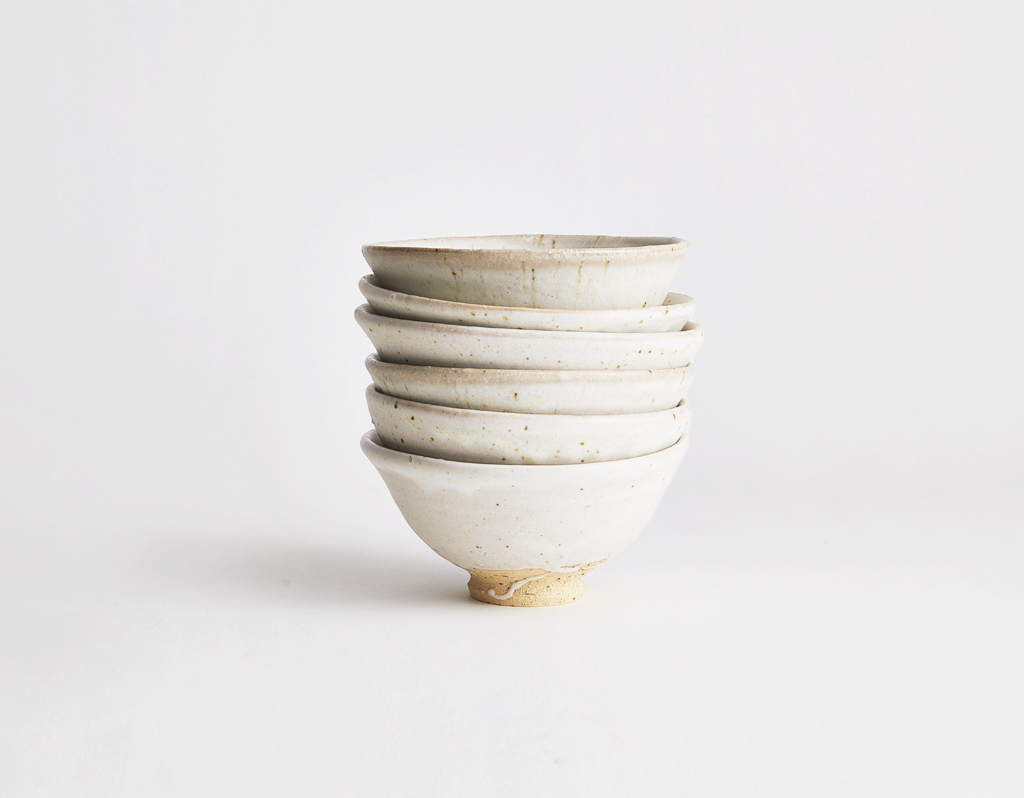 Six white glazed bowls by Keisuke Iwata, all stacked on top of each other on a gray background