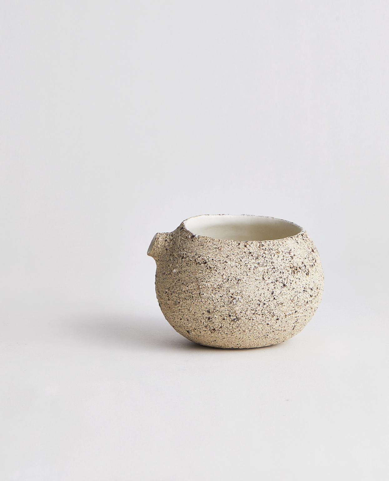Textural, egg-shaped katakuchi by Keisuke Iwata with a beige and black speckled exterior and a white interior on a gray background