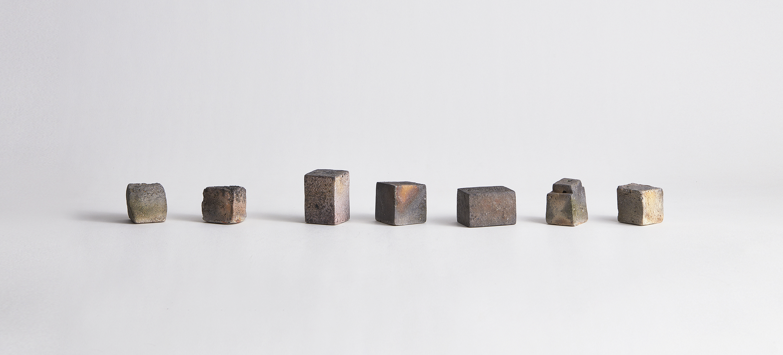 Seven sculptural rectilinear vases by Keisuke Iwata lined up on a gray background