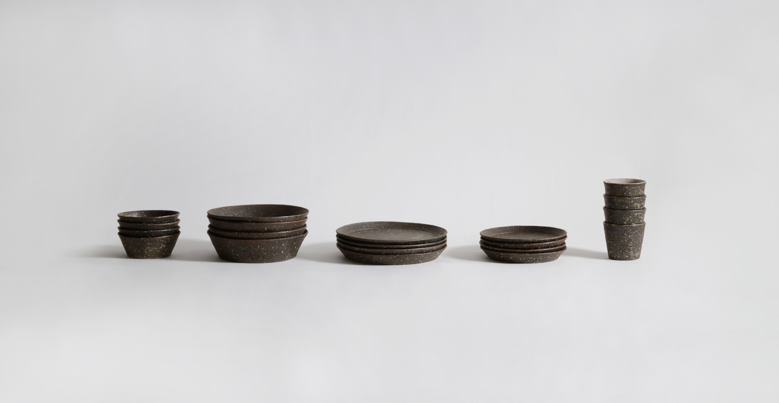 Stacked textured ceramic plates, cups and bowls in a row against gray background