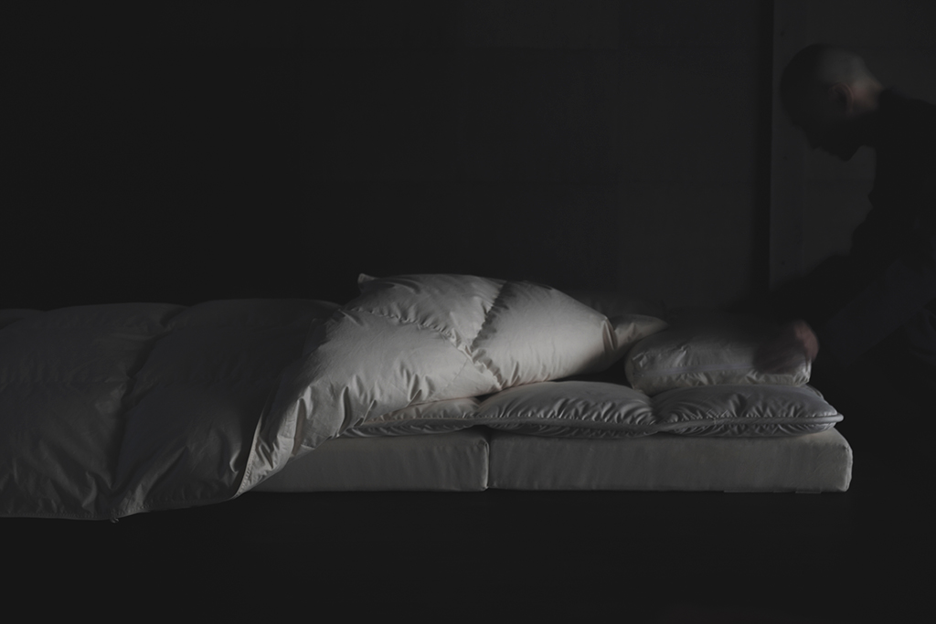 A person setting up their white futon setup in a dark room
