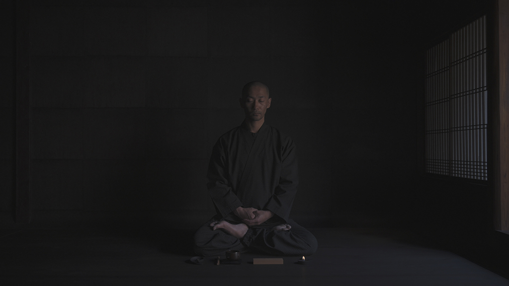 Calm meditative person sitting cross legged with eyes closed in a dark room
