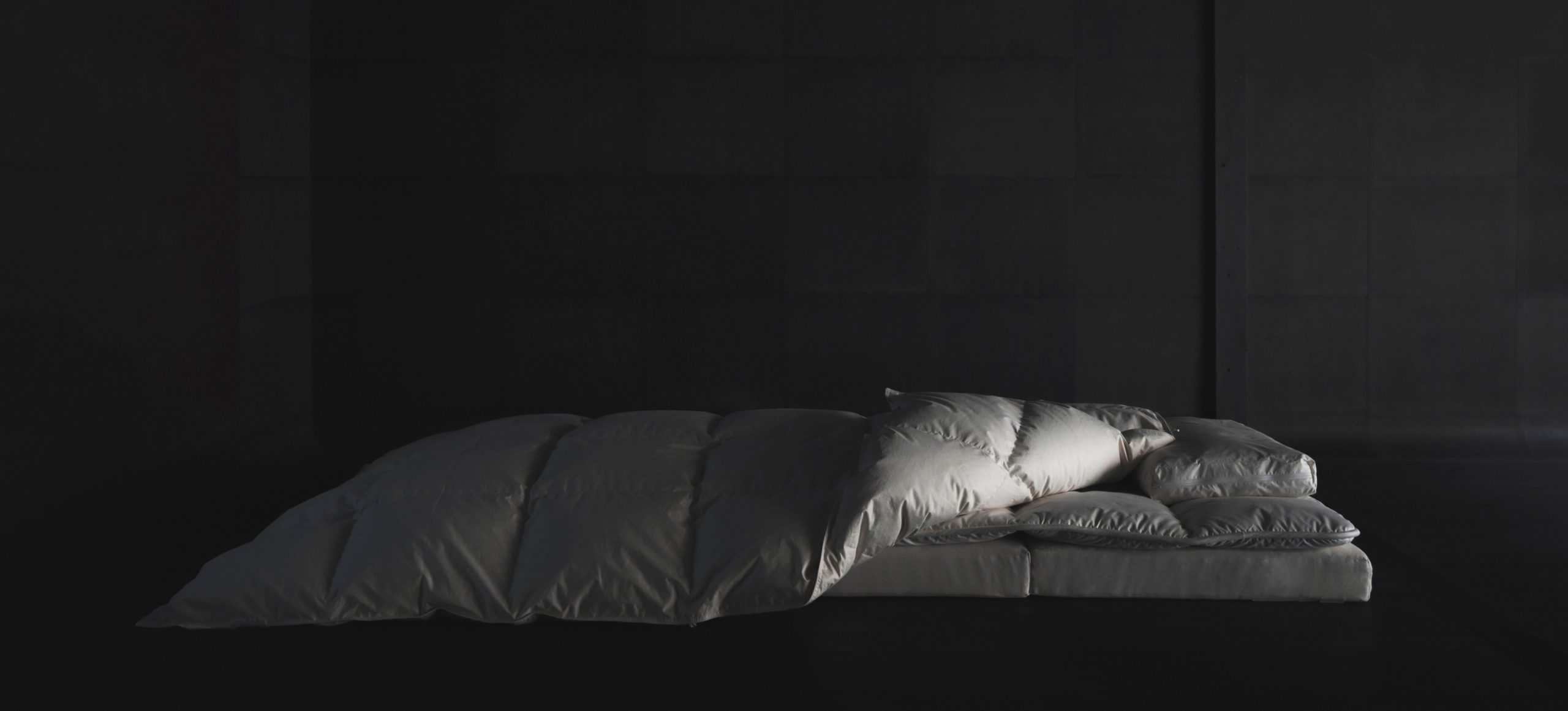 dark image of offwhite natural futon and fluffy down duvet blanket setup by Iwata Nezen laid out on the ground