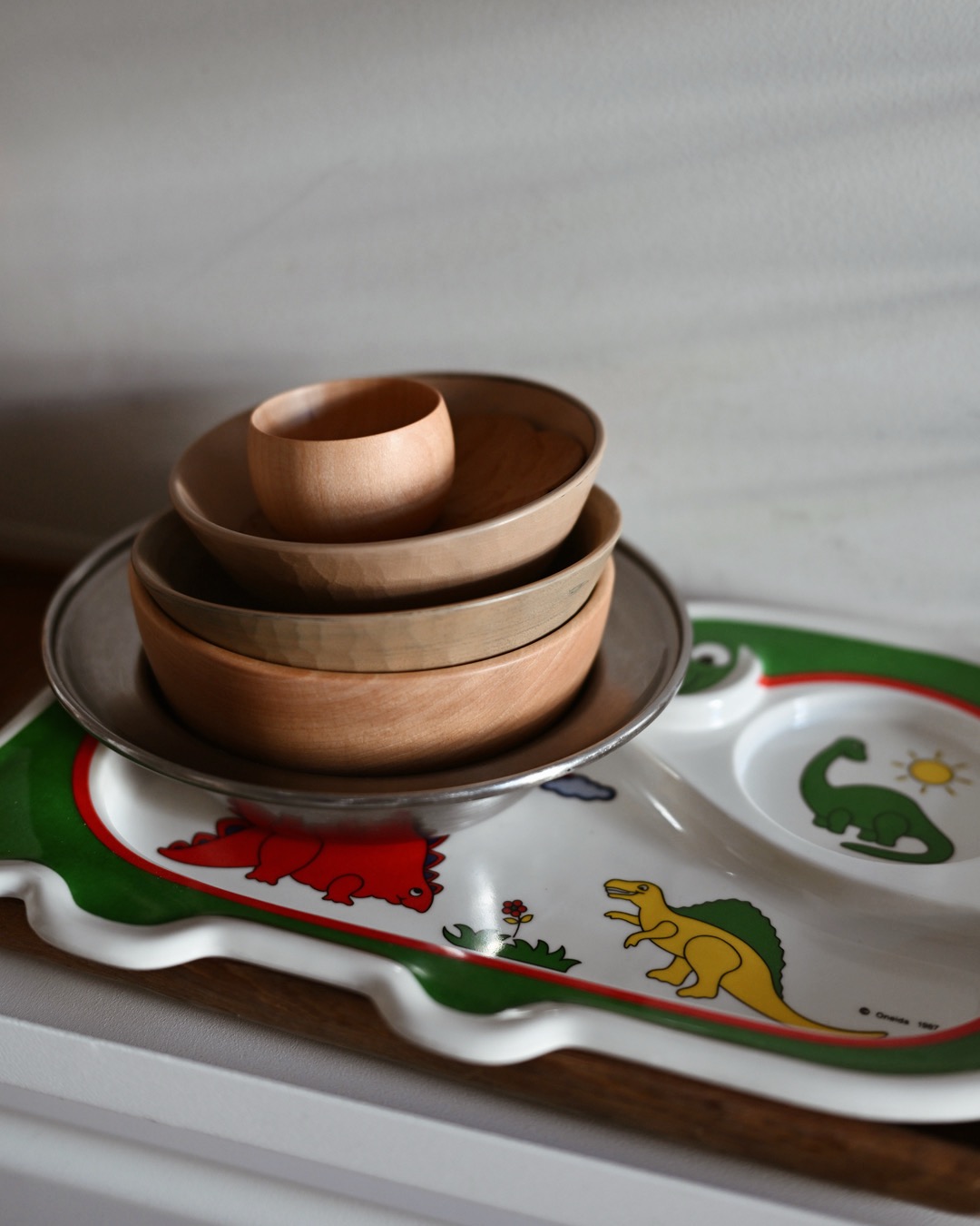 stack of wooden and stainless Kay Bojeson and Ryuji Mitani children's bowls on a vintage Oneida divider Dinosaur plate