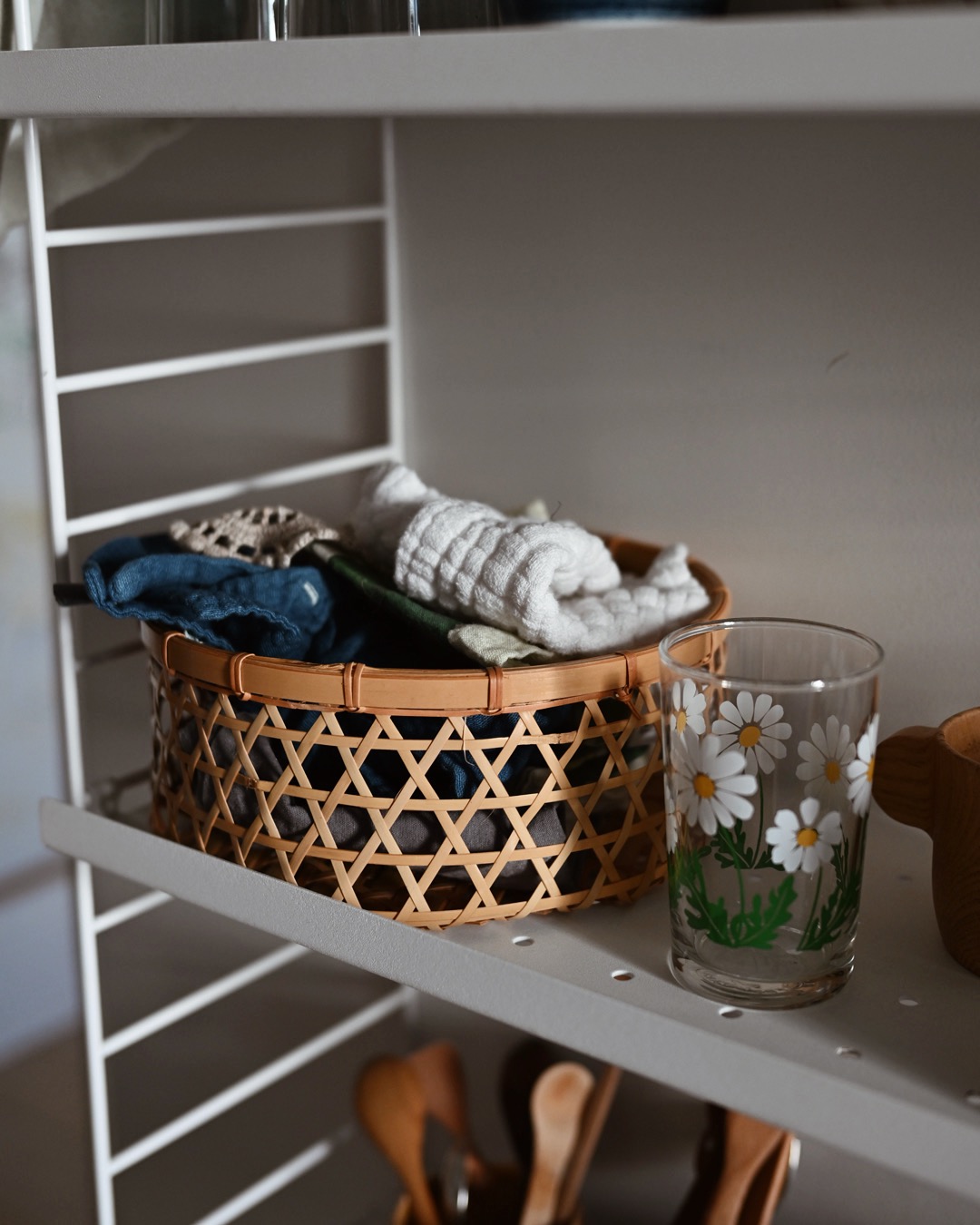 Cloths, bibs and knitted rose coasters in a bamboo woven basket resting on a shelf