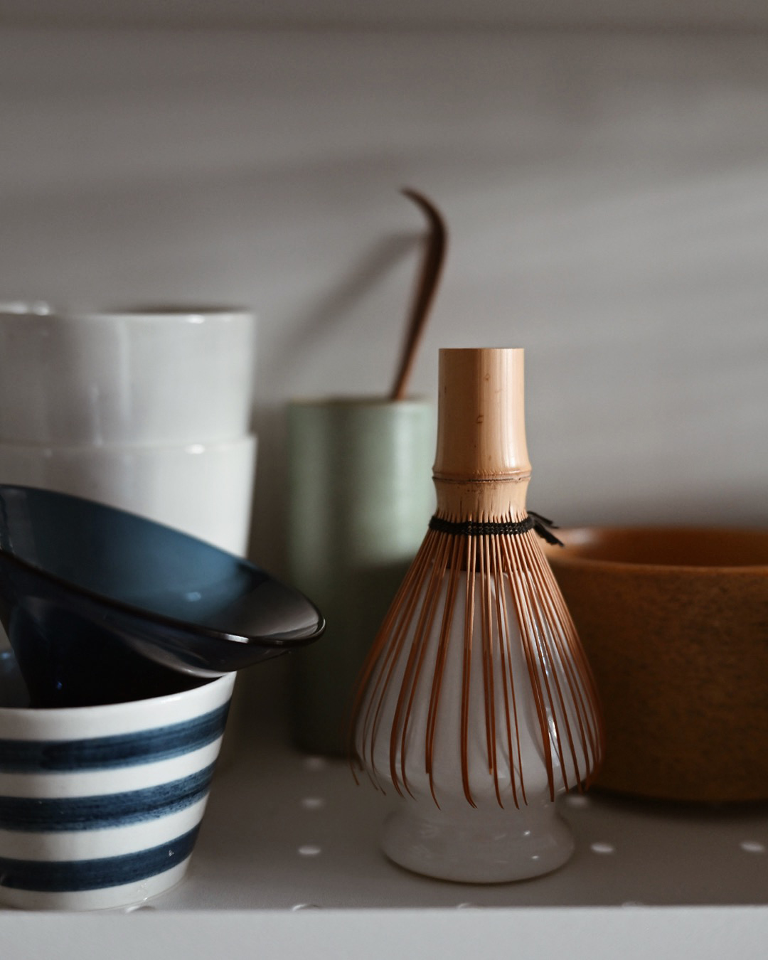Matcha bamboo tea whisk on a stand with cups and SImplicity matcha bowl surrounding it