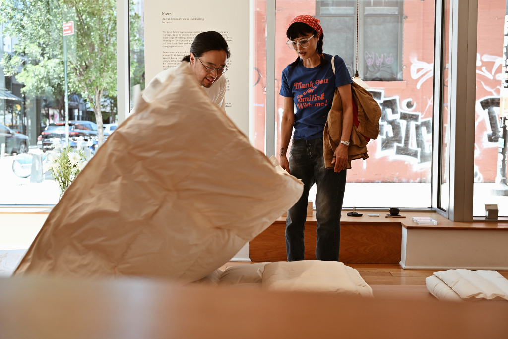 Man draping duvet by Iwata on futon set with a woman standing
