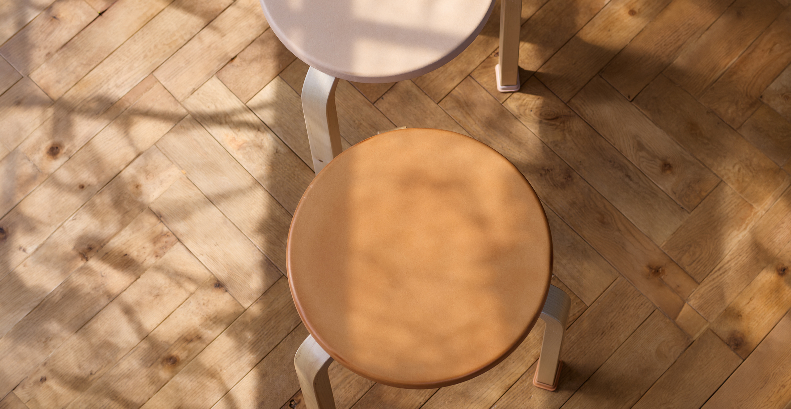 Hender Scheme + Artek natural vegetan leather covered stool with shoes with shadows and light dancing on them